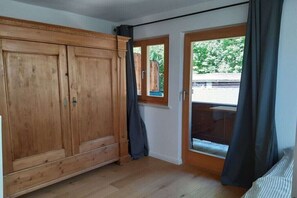 Ein Zimmer mit Holzschrank, Schiebeglasfenster und Blick ins Grüne.