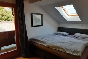 Ein Schlafzimmer mit Oberlicht, einem Bett mit gestreifter Bettwäsche, einem gerahmten Bild an der Wand und Blick ins Freie.