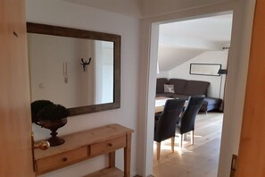 A room with a wooden console table, a mirror, and a potted plant. There is a doorway leading to another room with a sofa and a lamp. - Holiday apartment with 1 bedroom (Bad Wiessee)