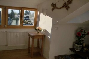 A room with a wooden table, a radiator, a window with a view, and a wall-mounted deer antler decoration. - Holiday apartment with 1 bedroom (Bad Wiessee)