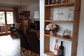 A living room with a sofa, chairs, a TV, and a wooden shelf with wine bottles and glasses. - Holiday apartment with 1 bedroom (Bad Wiessee)