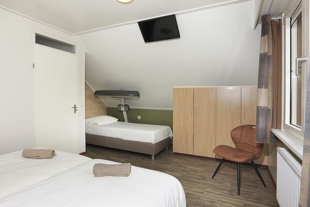A bedroom with a bed, a chair, a wardrobe, and a television.