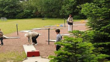 An outdoor recreational area with a shuffleboard table, a person playing shuffleboard, and another person observing.