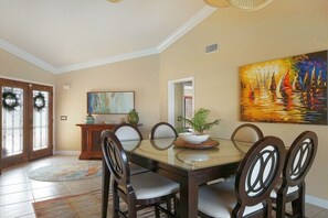 A dining area with a glass table, wooden chairs, a potted plant, and a painting on the wall. - Villa in Cape Coral with swimming pool (Cape Coral)