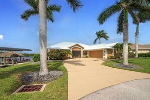 A residential property with a curved driveway, palm trees, and a well-maintained lawn. - Villa in Cape Coral with swimming pool (Cape Coral)