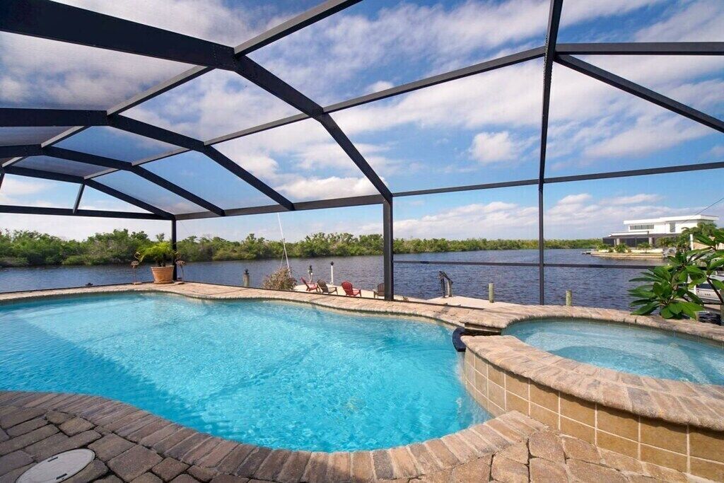 A swimming pool with a covered area, surrounded by a natural landscape and a body of water.