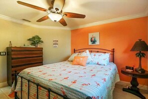 Ein Schlafzimmer mit einem Bett, einem Deckenventilator, einem Nachttisch, einer Lampe und einem an der Wand befestigten Regal.