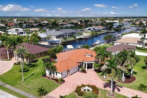 Un quartier résidentiel avec une grande maison dotée d’un toit rouge, entourée de palmiers et bordée d’un canal.