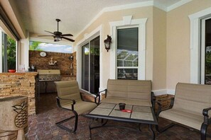 Eine Außenpatio mit Tisch und Stühlen, einem Deckenventilator und einer Steinmauer mit Grill.