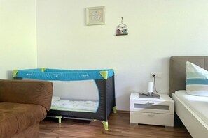 A bedroom with a bed, a nightstand, a small shelf with a decorative item, and a crib with a play mat. - Garden apartment Sonnalm - Apart Rauch (Ramsau)