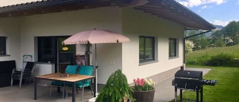 Une terrasse avec une table et des chaises, un barbecue et des plantes en pot.