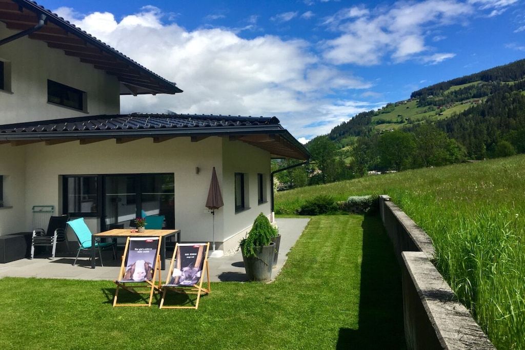 A two-story building with a patio area, outdoor seating, and a view of a green valley.