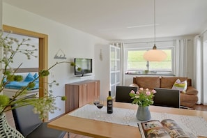 A modern living room with a dining area, a television, and a large window. - Garden apartment Sonnalm - Apart Rauch (Ramsau)