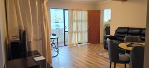 A living room with a sofa, a small table, and a TV. There is a sliding glass door leading to a balcony. - Calm and Private Lower Level Home in Mount Roskill (Auckland)
