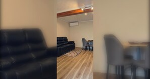 A living room with a black leather sofa, a dining table with chairs, and a patterned rug. - Calm and Private Lower Level Home in Mount Roskill (Auckland)