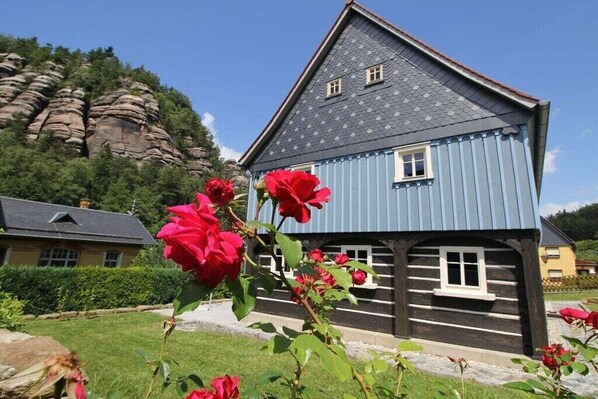 A blue wooden house with a sloped roof, surrounded by a garden with red roses. - Gebirgshäusl Oybin / Zittau Mountains (Oybin)