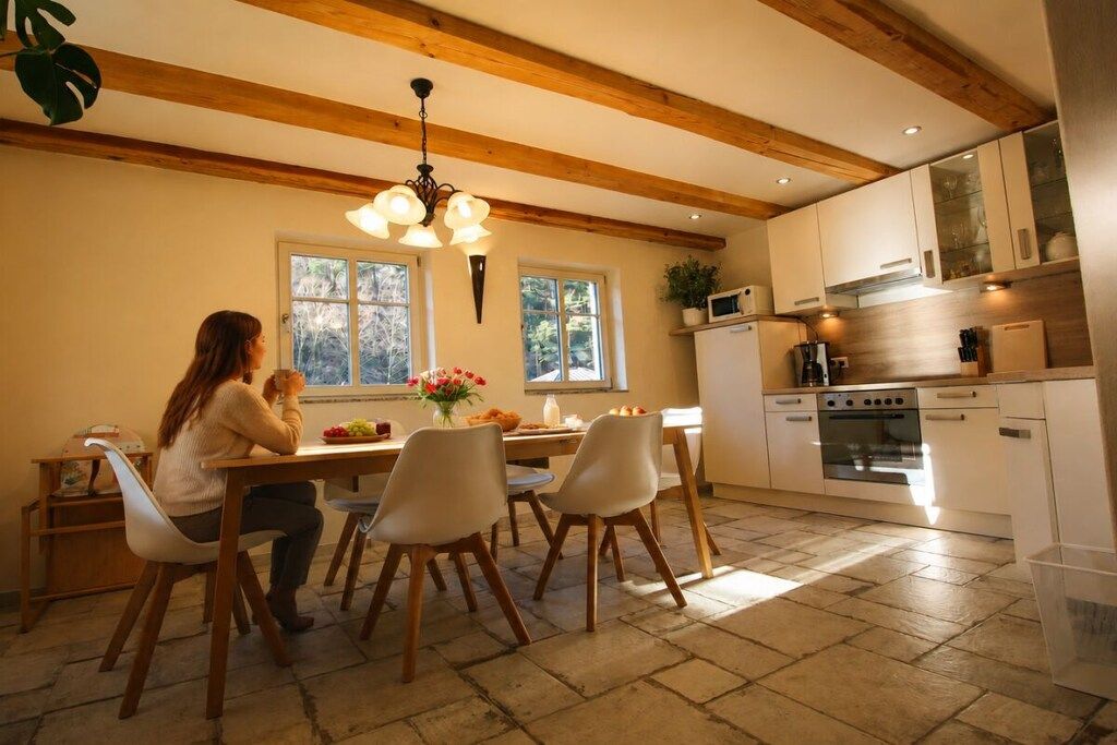 A dining area with a wooden ceiling, a chandelier, and a kitchen with white cabinets and appliances.