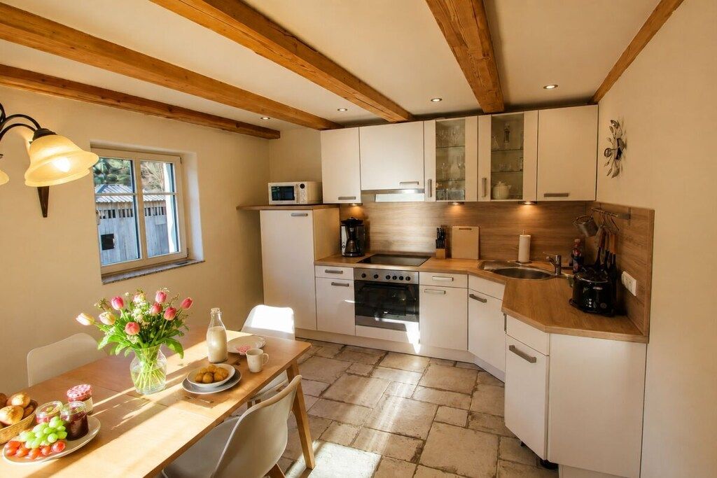 Cocina compacta con armarios blancos, microondas, estufa y lavabo. Hay una mesa de comedor con un jarrón de flores y un plato de comida.