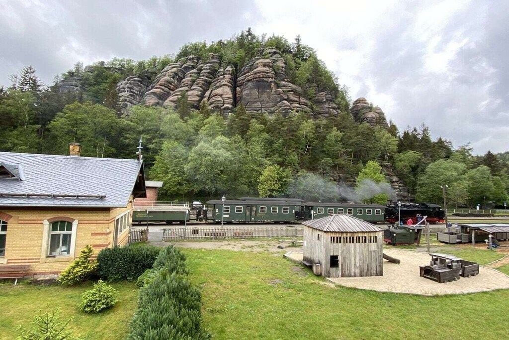 A train station with a green locomotive, a small wooden building, and a grassy area with trees.