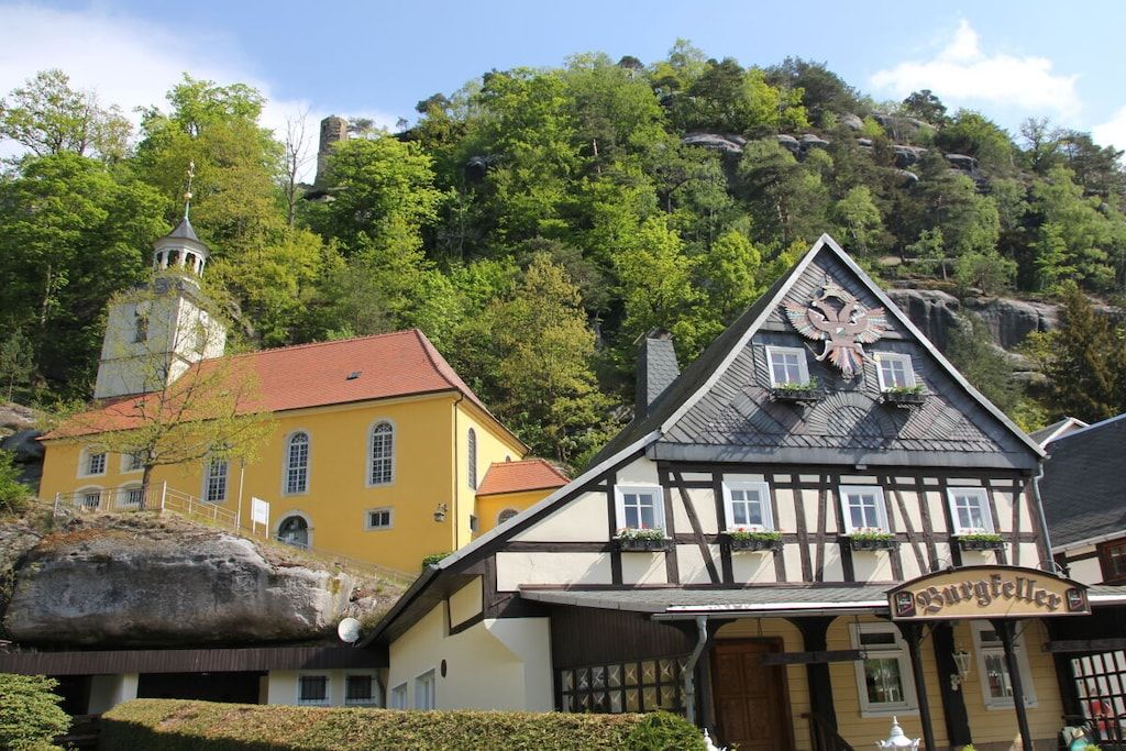 A traditional half-timbered building with a sign reading 'Burgsteller' in front of a yellow building with a red roof.