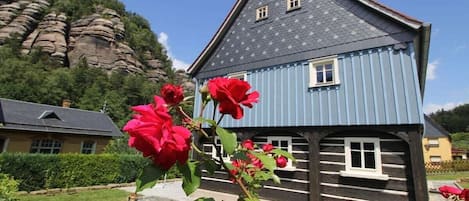 A traditional wooden house with a steeply pitched roof, a small window, and a stone wall in the background.