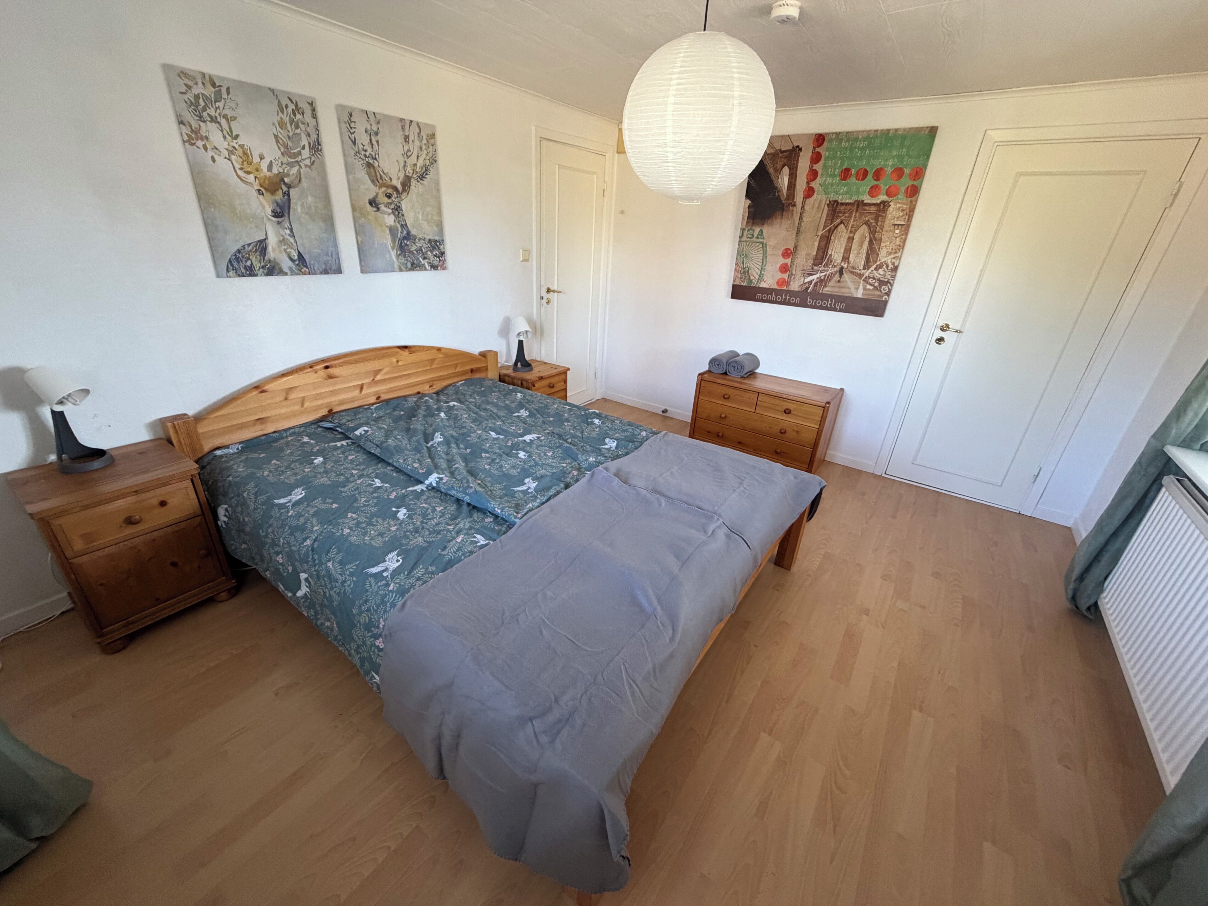 Une chambre à coucher avec un lit en bois, une table de chevet, une commode et un mur décoré d’œuvres d’art.