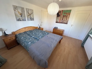 A bedroom with a wooden bed, a nightstand, a dresser, and a wall with artwork.