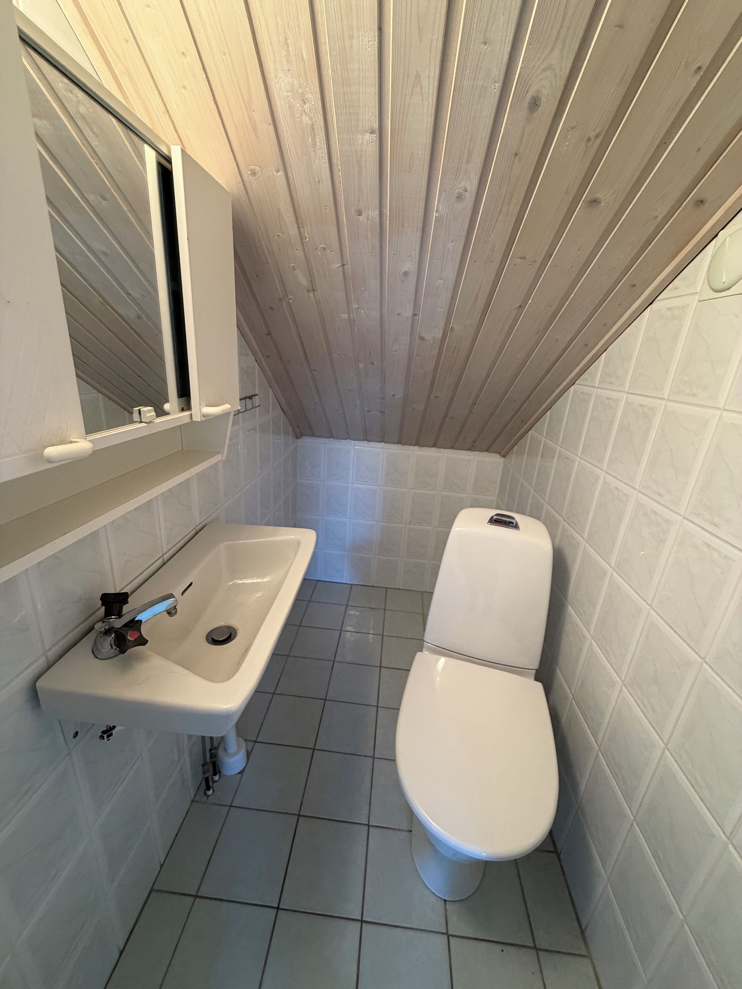 A small, compact bathroom with a white sink, a toilet, and a mirror above the sink.