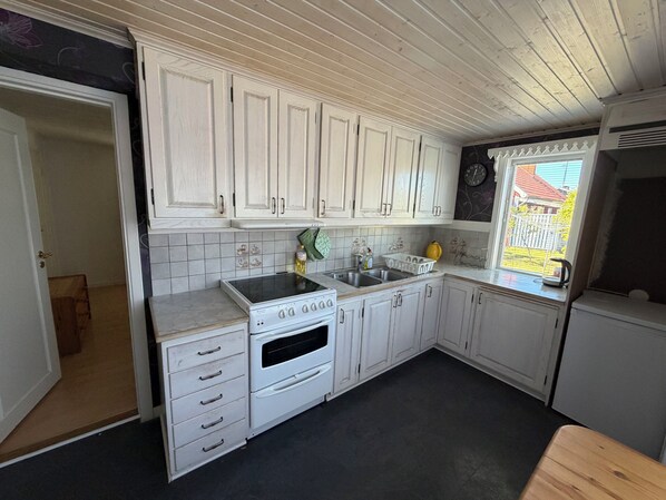 A kitchen with white cabinets, a stove, a sink, and a window with a view of the outside.