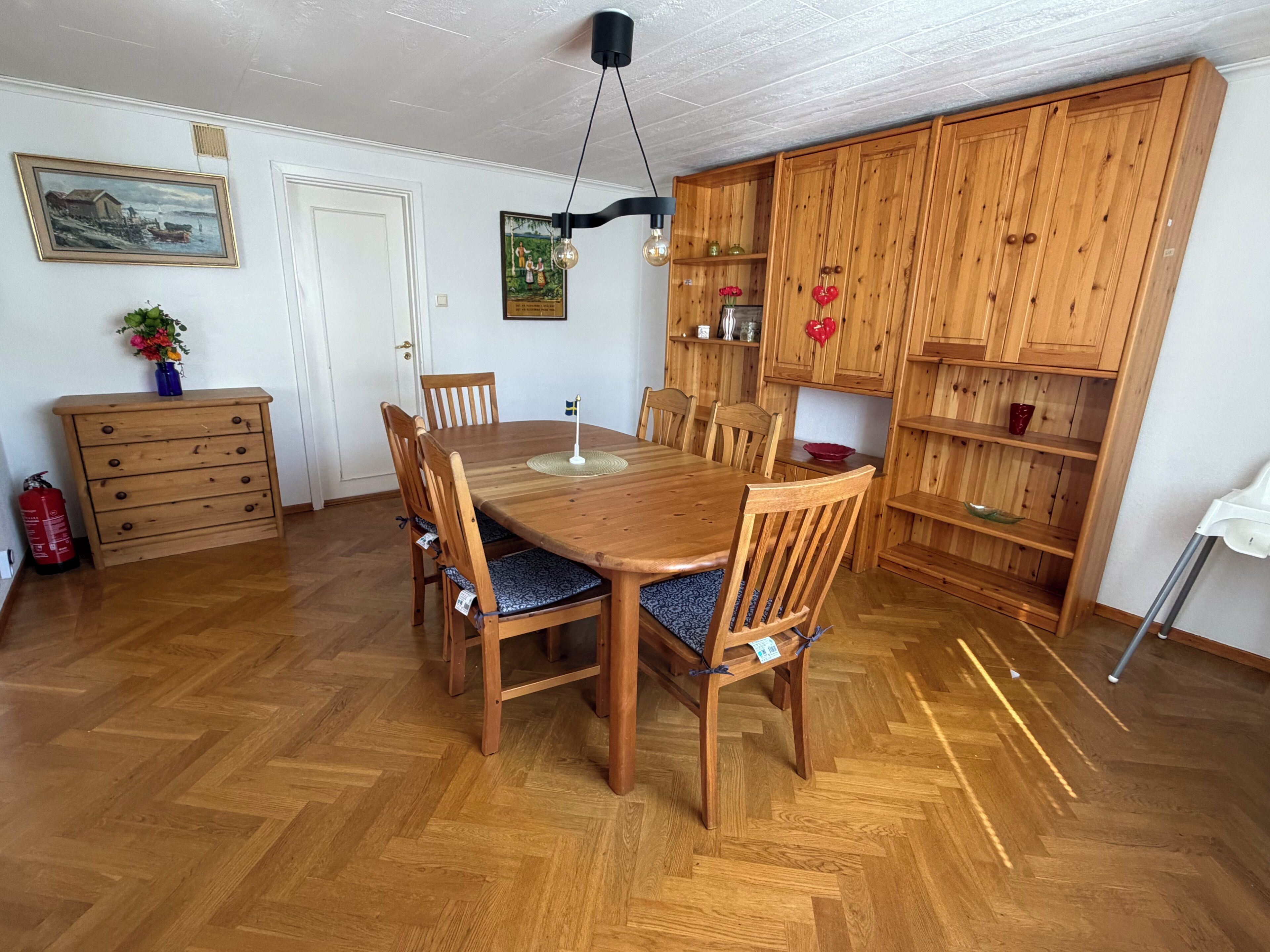 Un coin repas avec une table et des chaises en bois, un meuble en bois doté d’étagères et un extincteur.