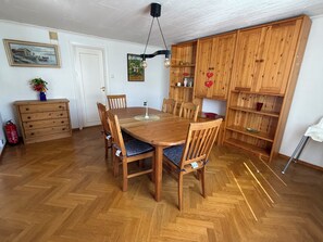 A dining area with a wooden table and chairs, a wooden cabinet with shelves, and a fire extinguisher.