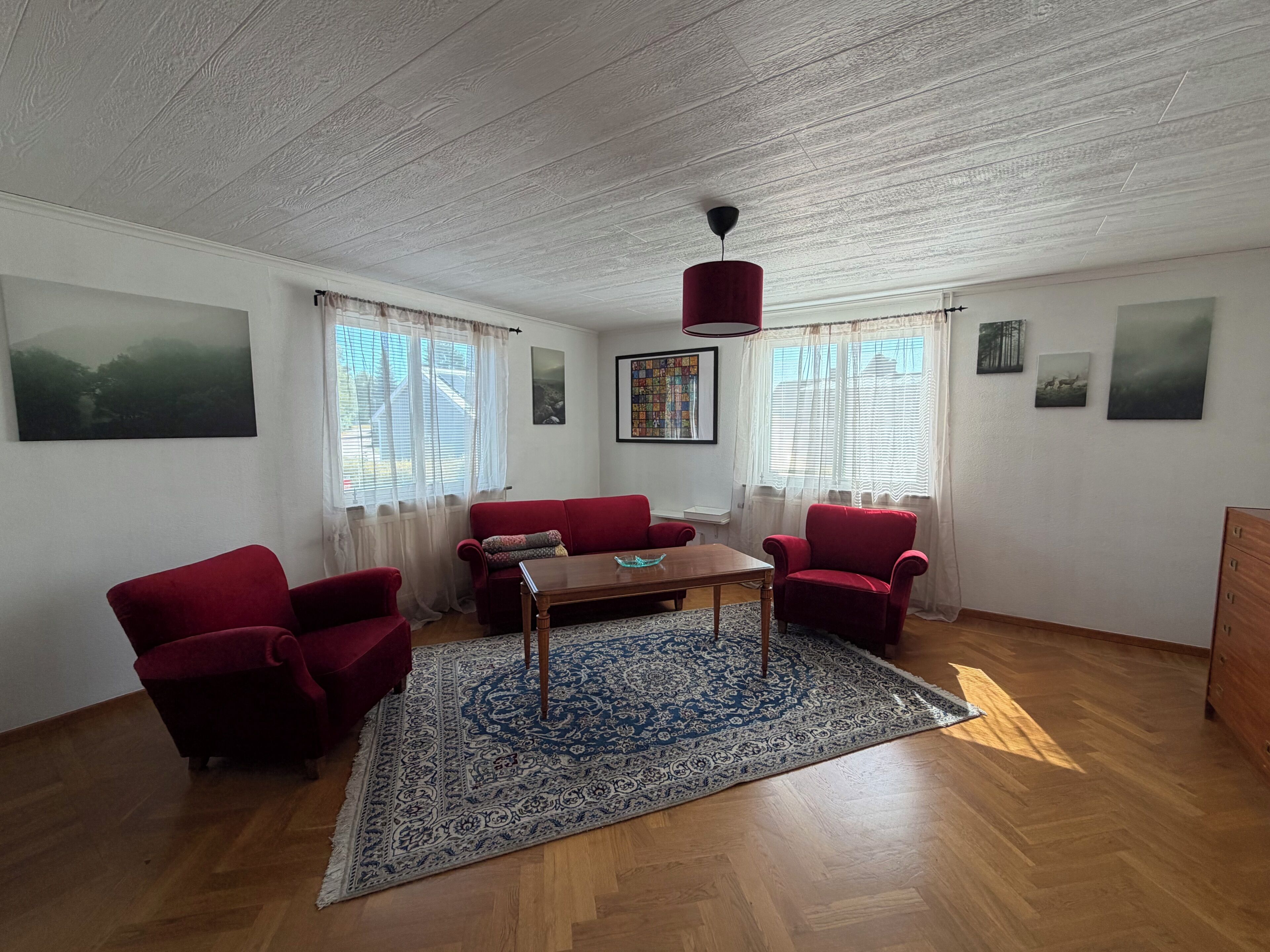 Un salon spacieux avec un canapé rouge, une table basse en bois et un tapis à motifs.
