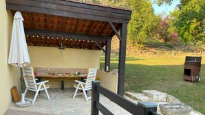 Une terrasse extérieure dotée d’une pergola en bois, d’un sol en pierre et d’une table dressée pour les repas.
