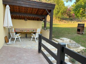 Eine Terrasse im Freien mit einer Holzw pergola, Steinböden und einem Esstisch.