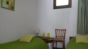 A room with two single beds, a desk with a chair, a window, and a painting on the wall.