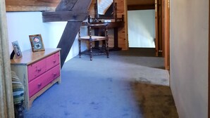A room with a sloped ceiling, a wooden chair, a dresser, and a framed picture.