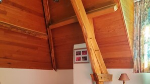 Une chambre avec deux lits, des poutres apparentes en bois au plafond, une petite table avec une lampe et une fenêtre avec des rideaux.