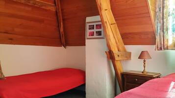 Une chambre avec deux lits, des poutres apparentes en bois au plafond, une petite table avec une lampe et une fenêtre avec des rideaux.