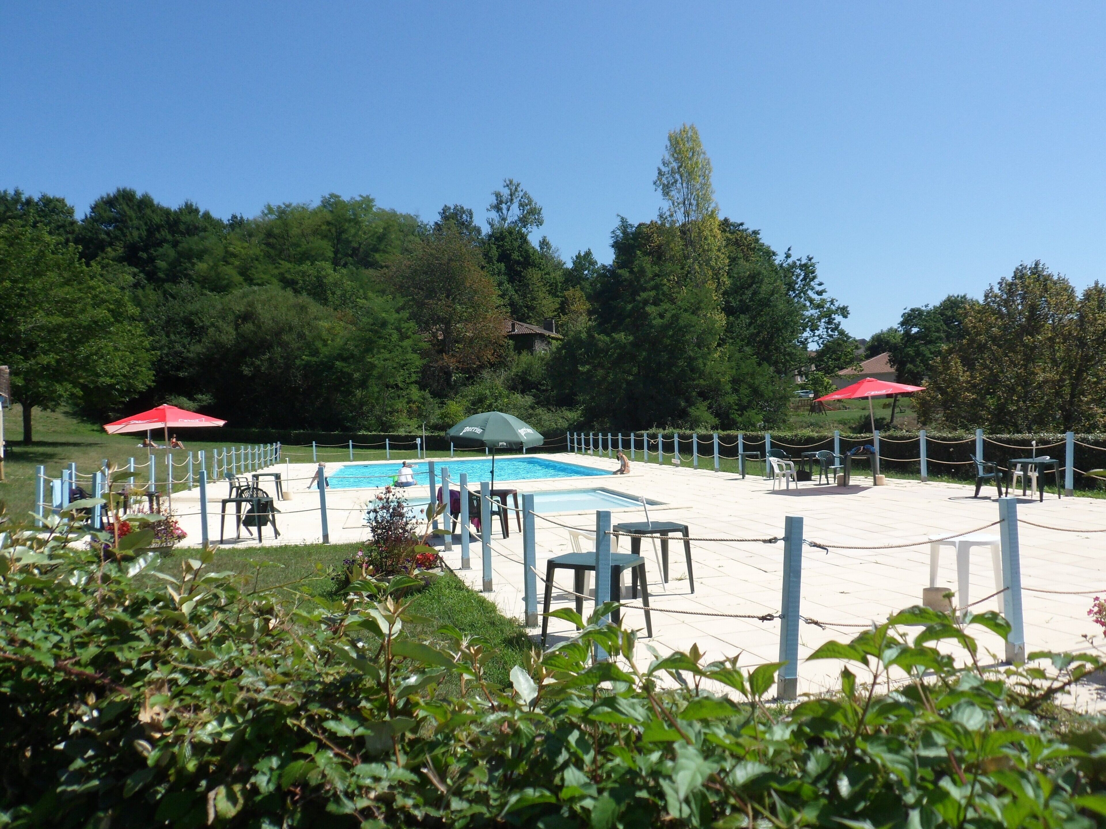 Un espace piscine entouré d’une clôture, avec des chaises et des parasols.