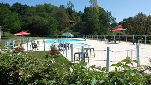 Un espace piscine entouré d’une clôture, avec des chaises et des parasols.