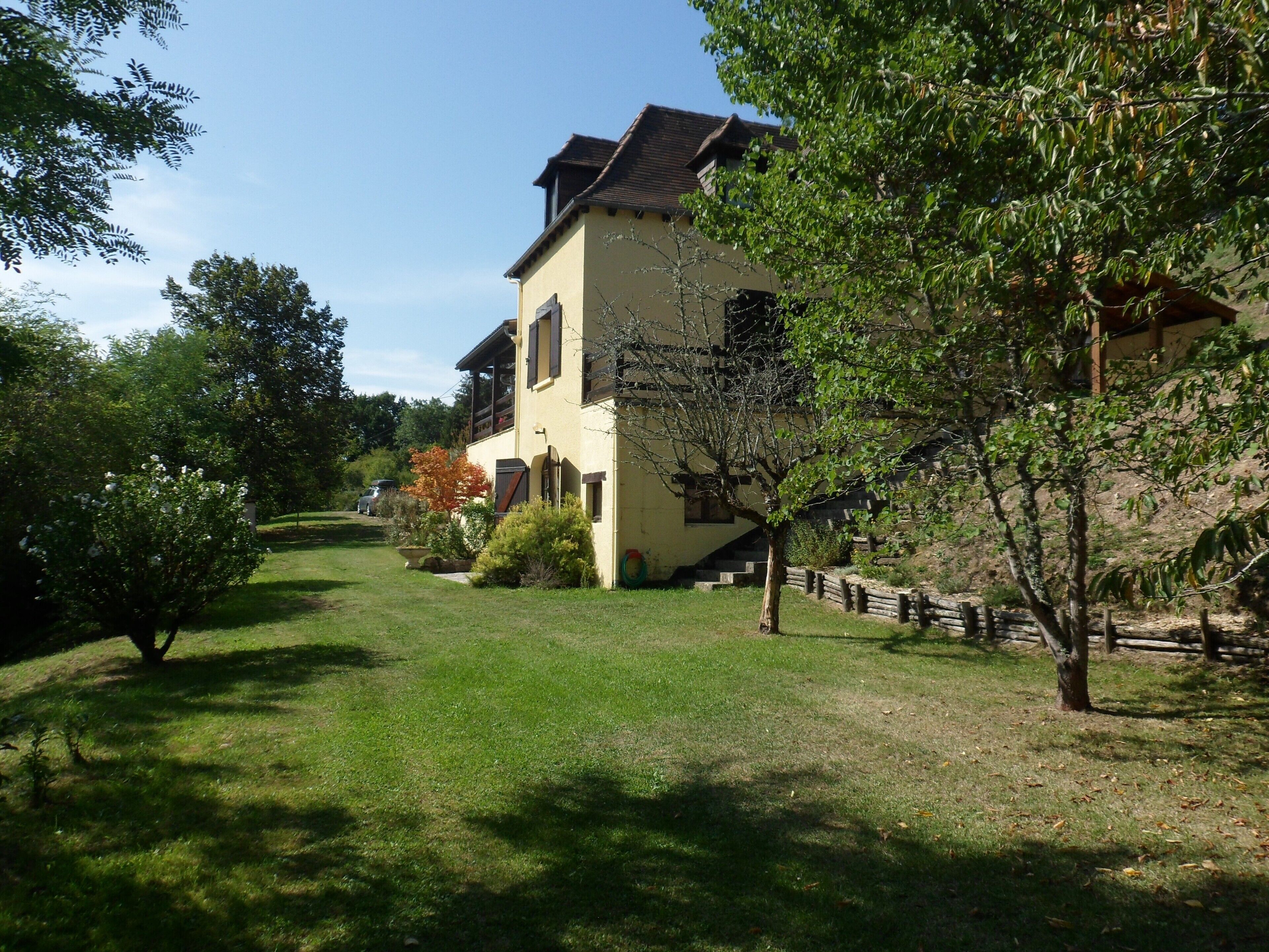 Une maison à deux étages, avec un toit en pente, un porche à l’avant et un petit jardin devant.