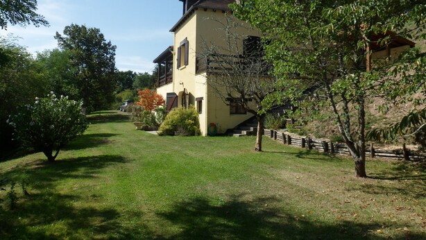 Une maison à deux étages, avec un toit en pente, un porche à l’avant et un petit jardin devant.