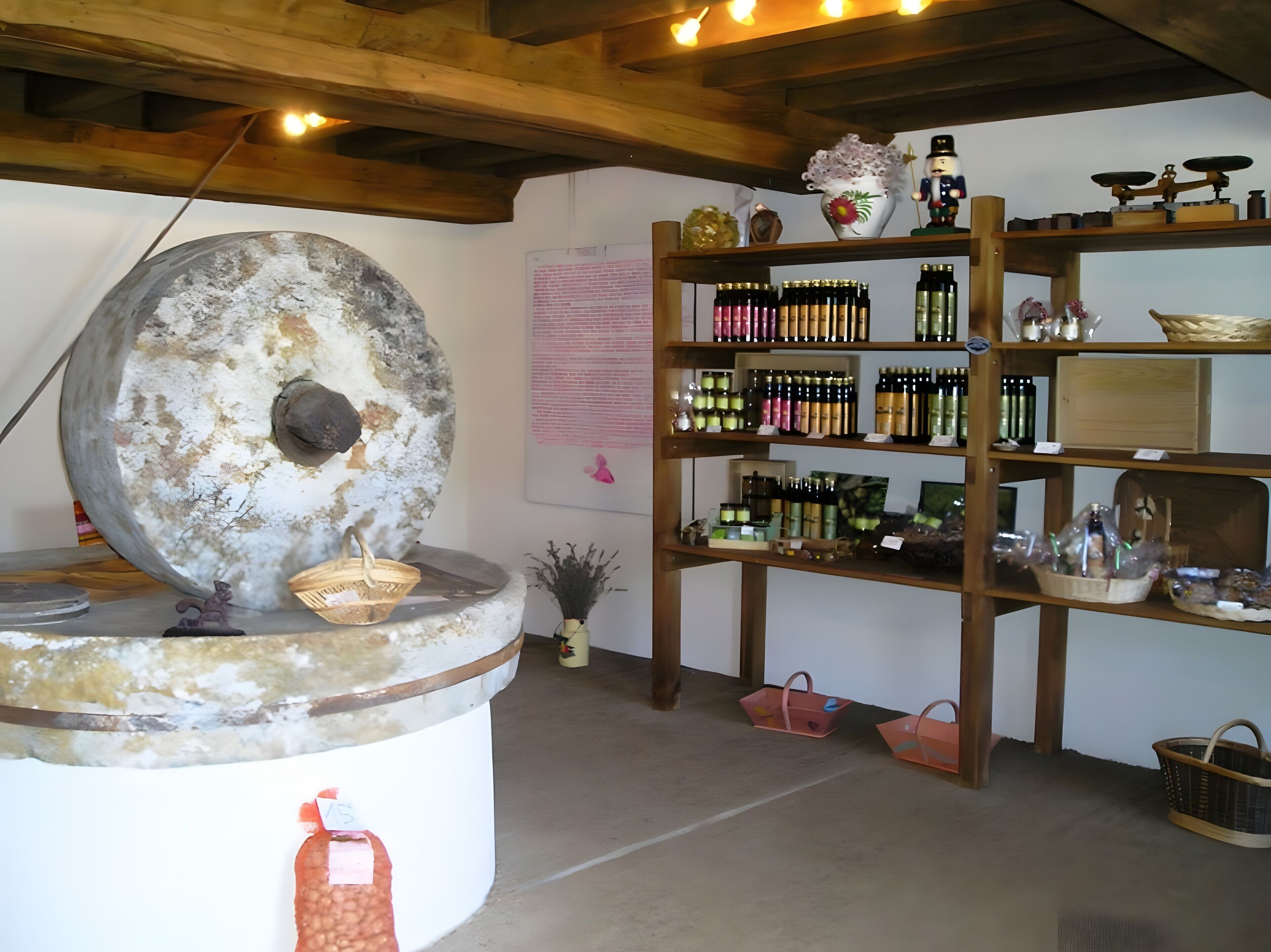 A rustic interior with a large stone mill, wooden shelves with bottles, and a brick wall.