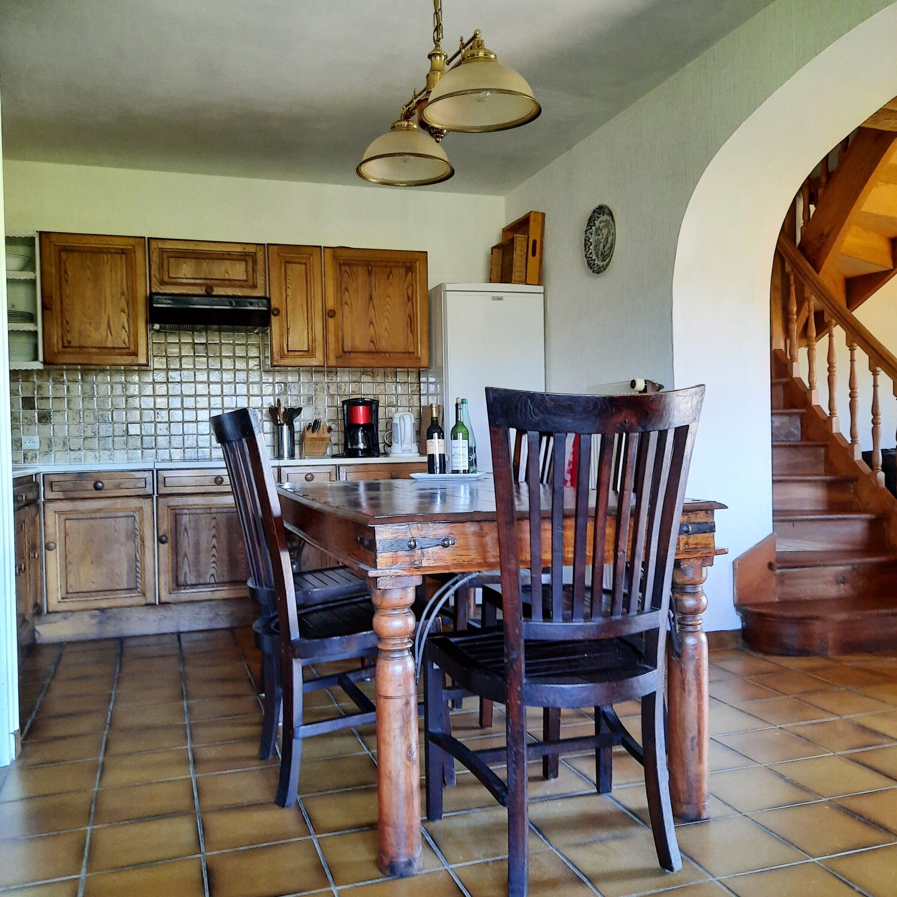 Une cuisine avec des meubles de rangement en bois, une table à manger, des chaises et un escalier.