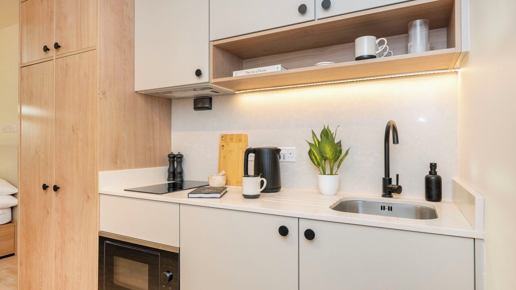 Eine moderne Küche mit Backofen, Kaffeemaschine, Wasserkocher und einem Topf mit Pflanze.