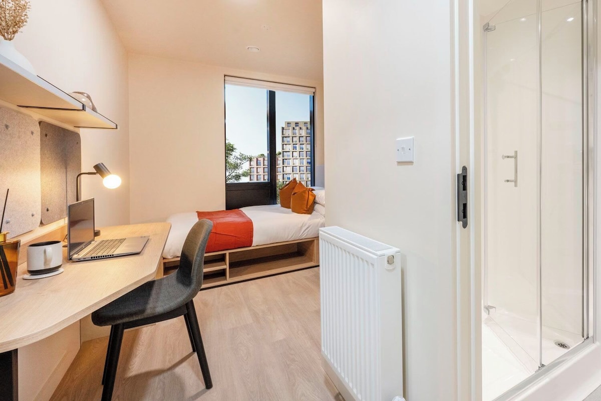 Une chambre moderne avec un lit, un bureau avec un ordinateur portable, une chaise et un radiateur.