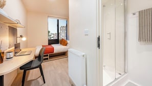 Une chambre moderne avec un lit, un bureau avec un ordinateur portable, une chaise et un radiateur.