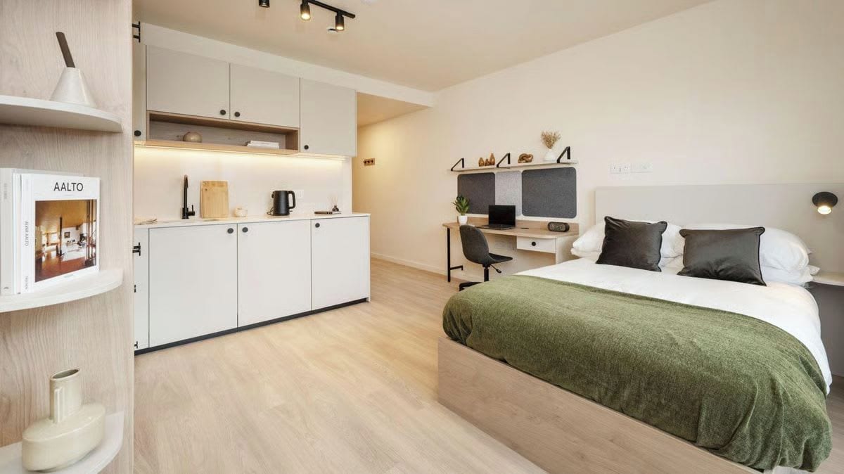 A modern bedroom with a bed, a desk, and a kitchenette area.