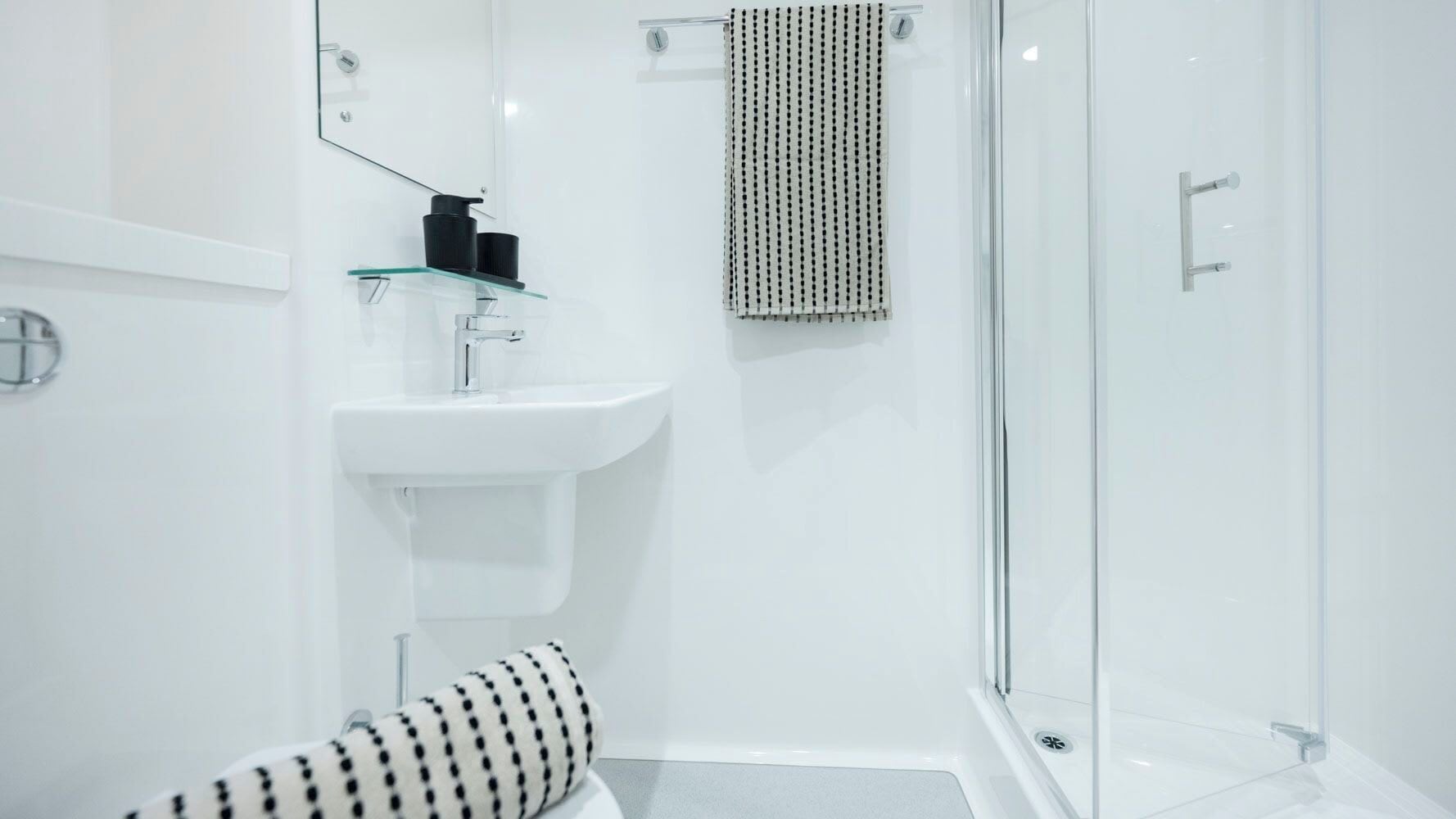 A modern bathroom with a glass shower enclosure, a white sink, and a black and white patterned towel.