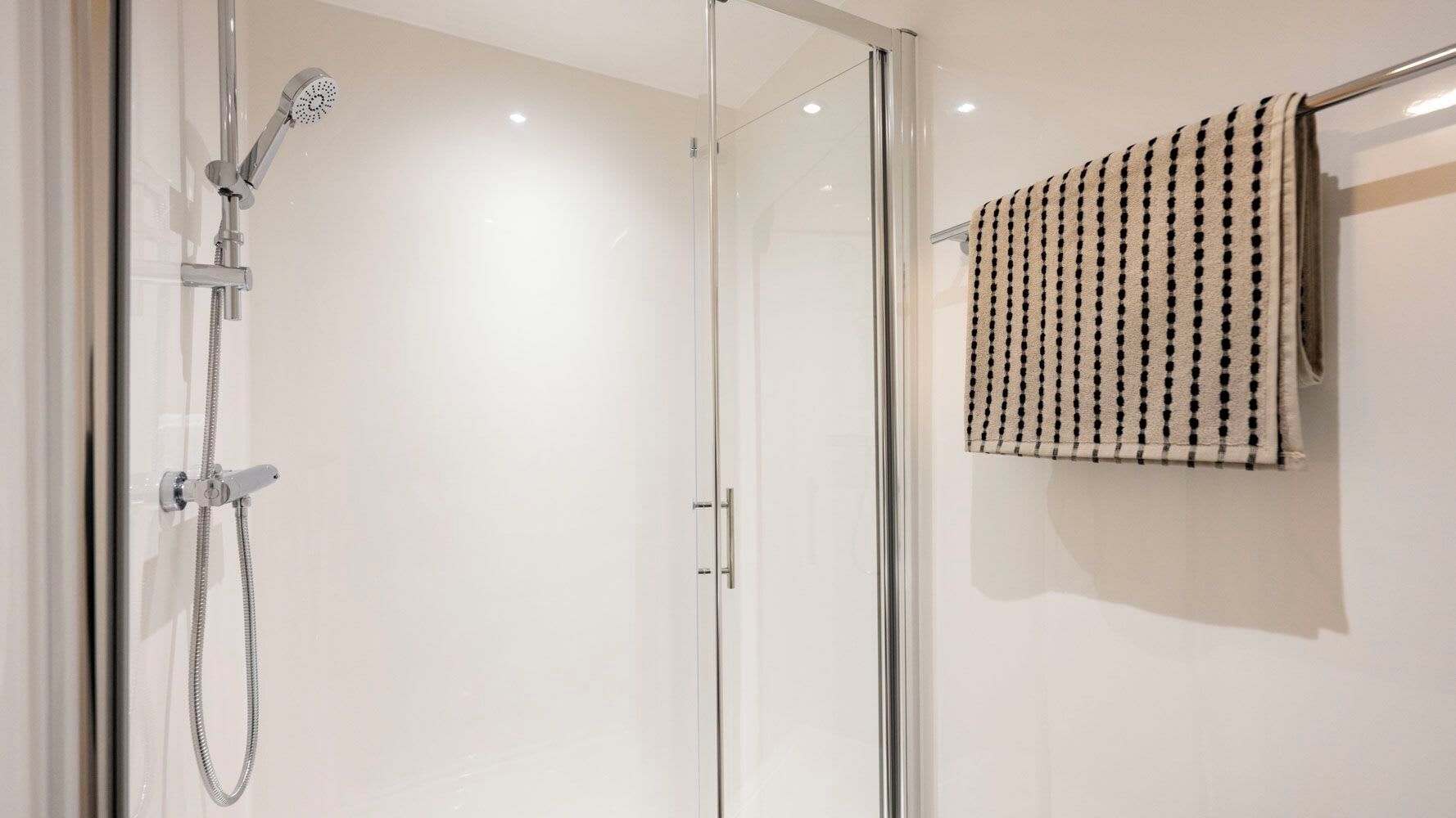 A modern bathroom with a glass shower enclosure, a towel rack with a striped towel, and a visible shower control panel.